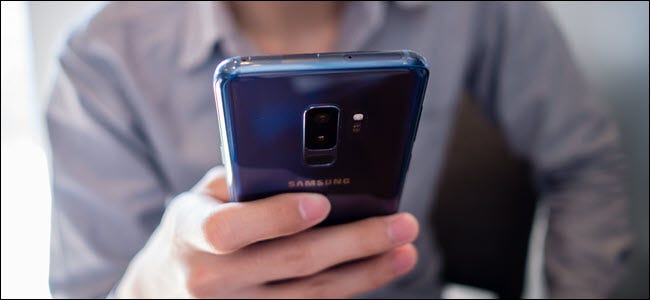 mężczyzna w szarej koszuli używa niebieskiego Samsunga S9 plus