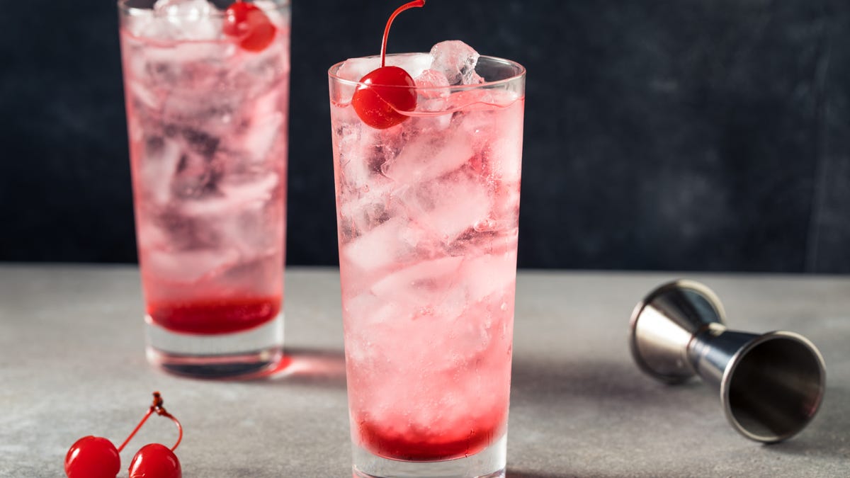 Dwa różowe drinki stoją w wysokich szklankach z wisienką na wierzchu.