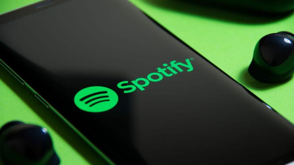 spotify logo on a smartphone next to truly wireless earbuds